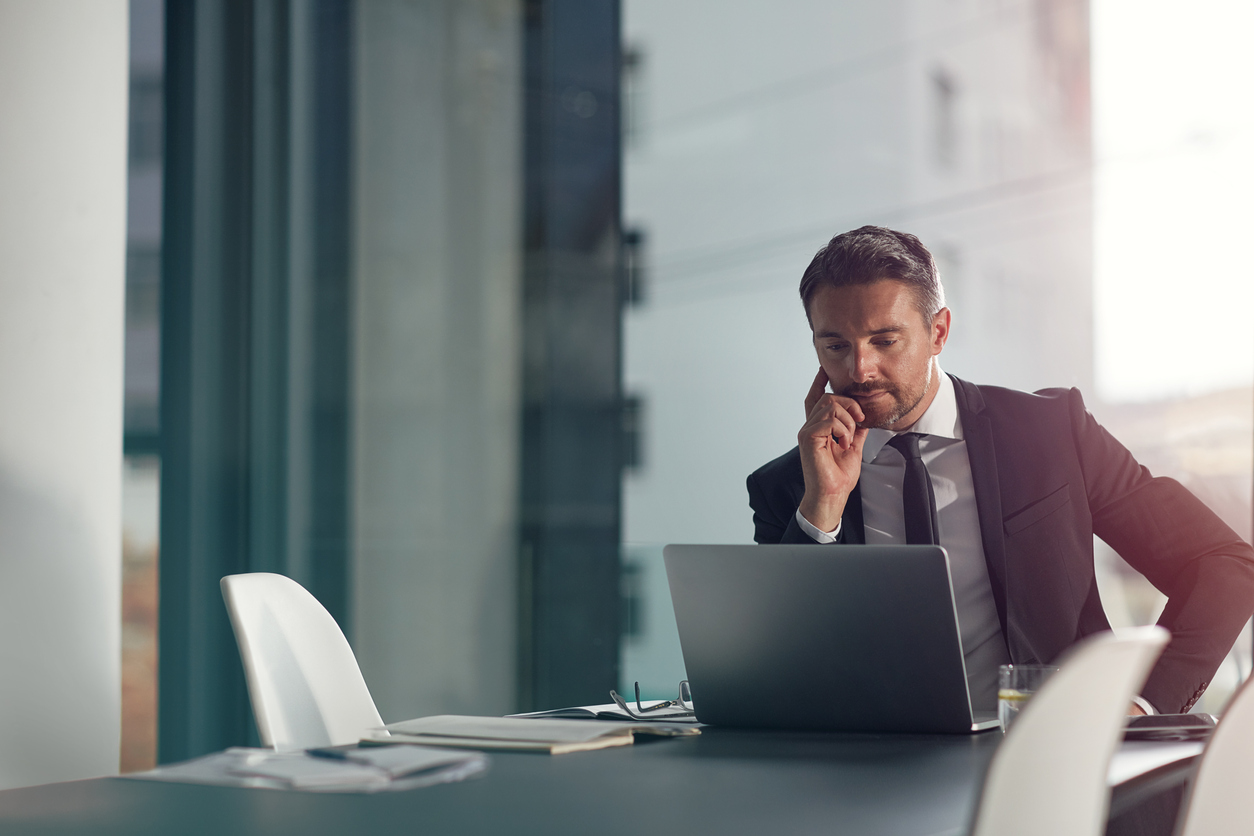 A businessman at a laptop in a quiet office, thinking through an insurance procurement decision